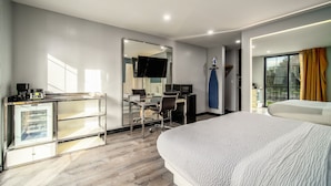 Een moderne hotelkamer met een groot bed, een bureau met computer, een kleine kitchenette en uitzicht op het omliggende landschap.