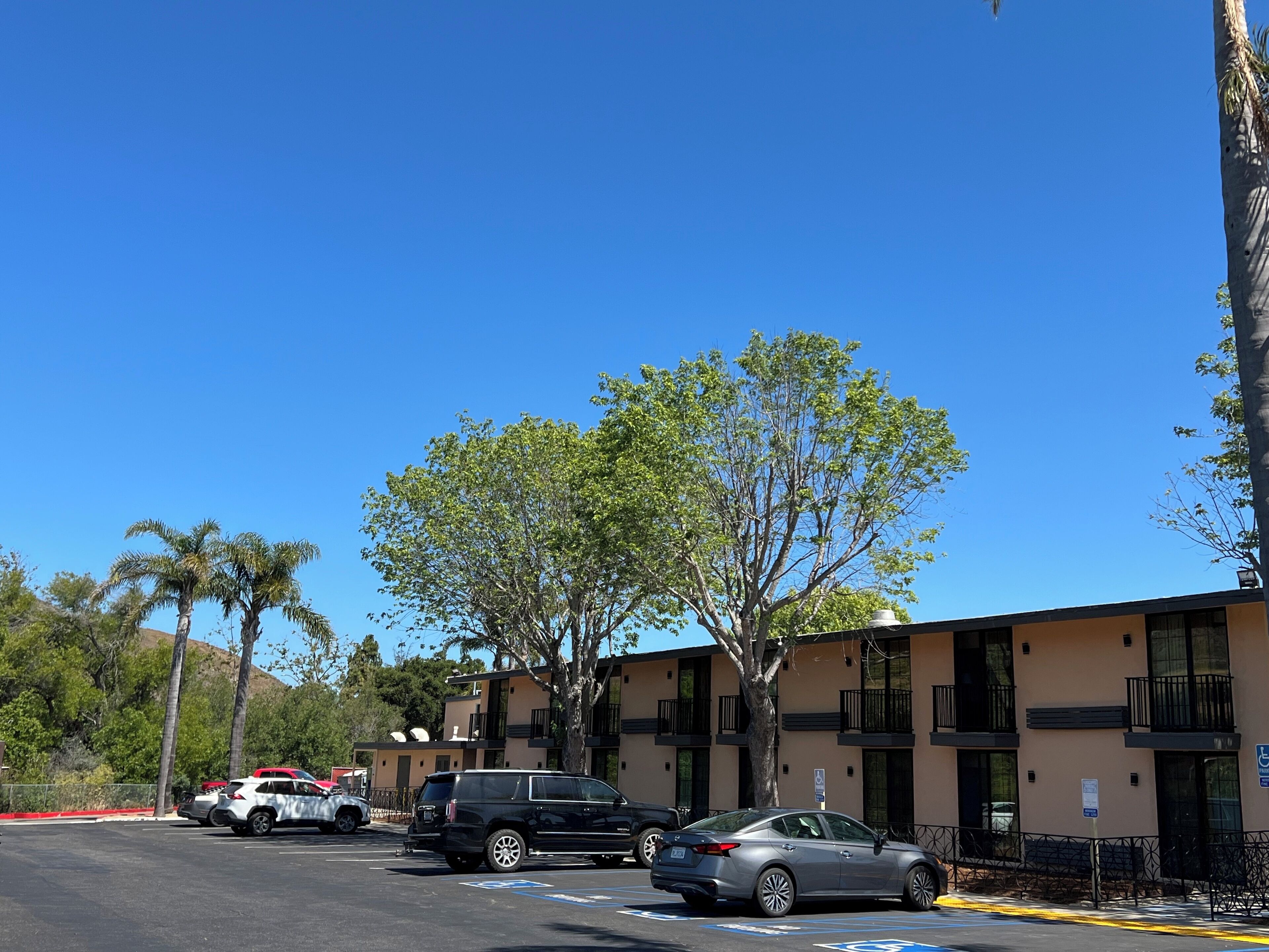 A parking lot with several cars, a building with balconies, and trees.