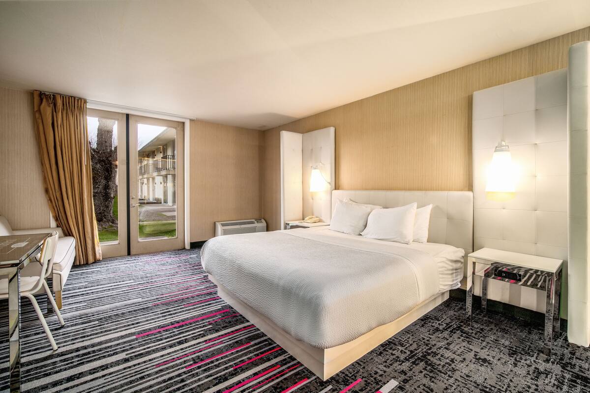 Une chambre d’hôtel avec un grand lit, un bureau avec une chaise, une table de chevet, une lampe et une vue sur l’extérieur.