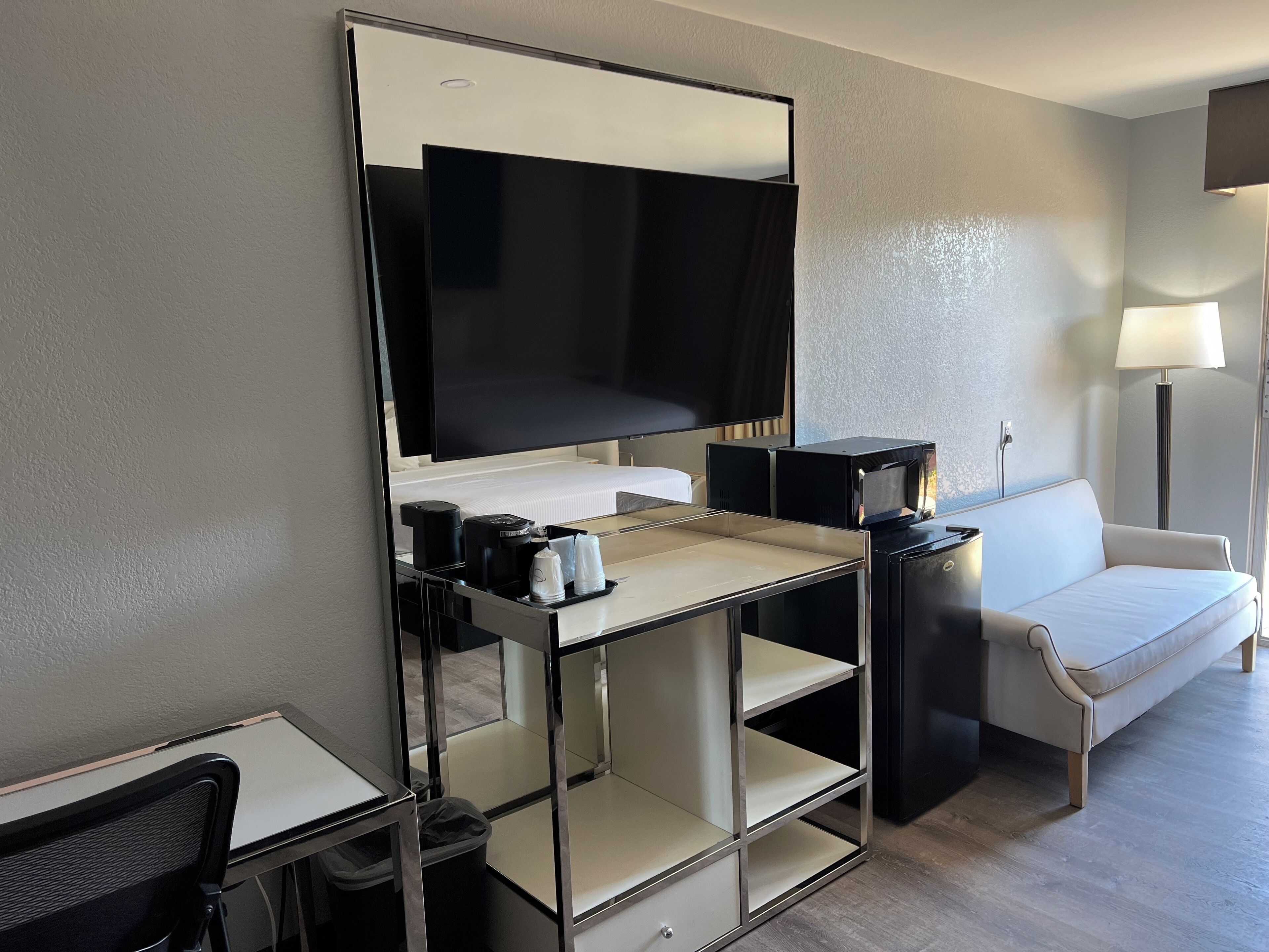 Une chambre d’hôtel équipée d’un bureau, d’une chaise, d’un lit, d’un canapé, d’une télévision, d’une machine à café et d’une lampe.