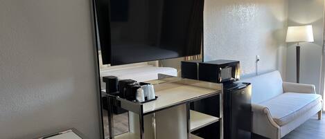 Une chambre d’hôtel équipée d’un bureau, d’une chaise, d’un lit, d’un canapé, d’une télévision, d’une machine à café et d’une lampe.