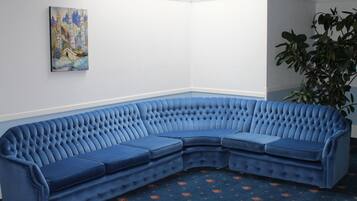 A corner room with a blue sectional sofa, a painting on the wall, and a potted plant.