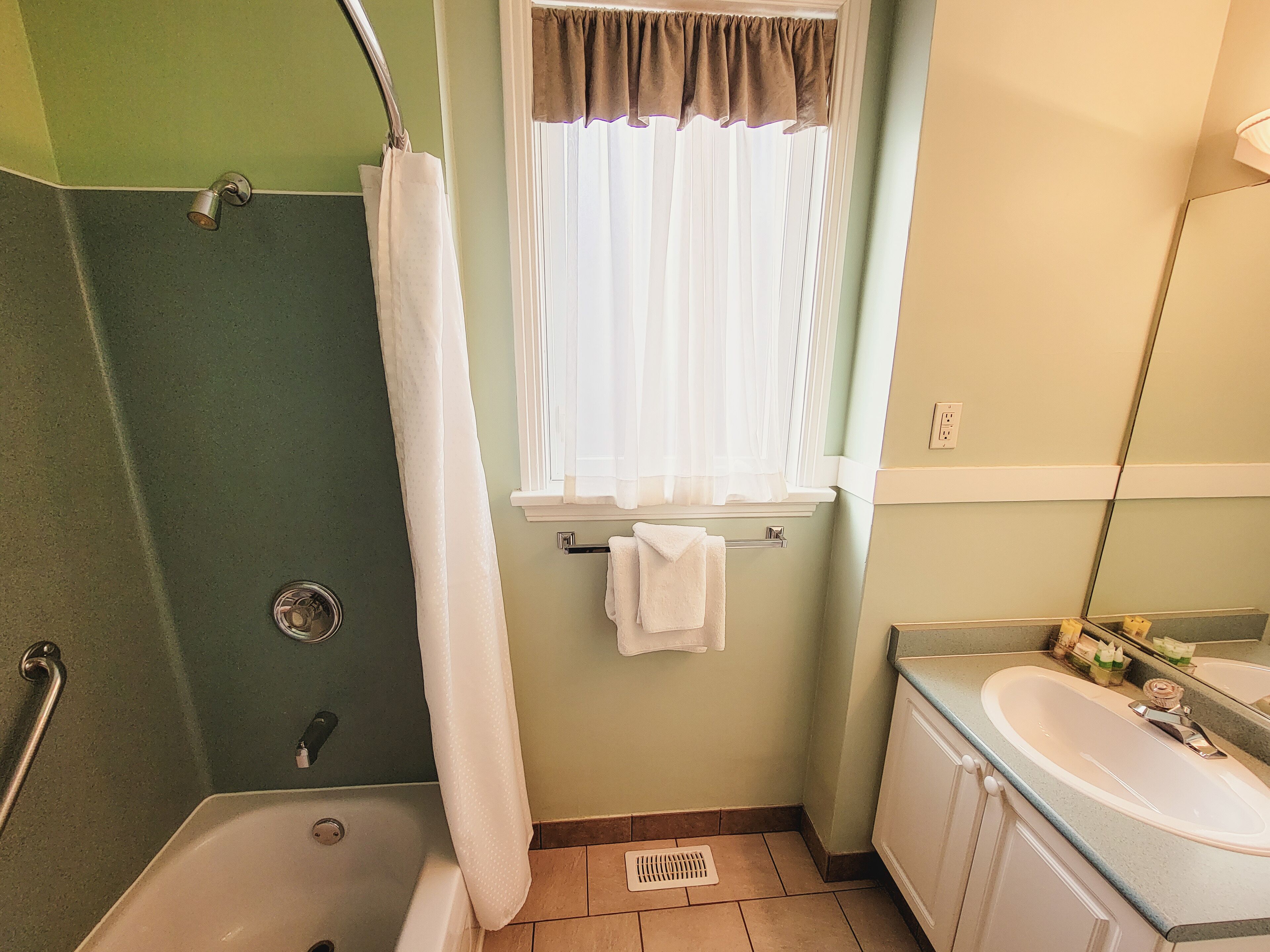 A bathroom with a shower, a sink, and a window with curtains.