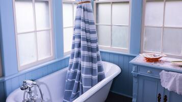 A bathroom with a clawfoot bathtub, a window with a striped curtain, and a vanity with a towel on it.
