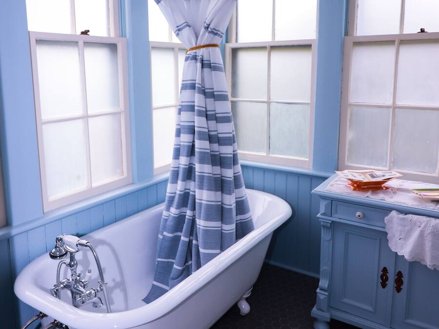 A bathroom with a clawfoot bathtub, a window with a striped curtain, and a vanity with a towel on it.