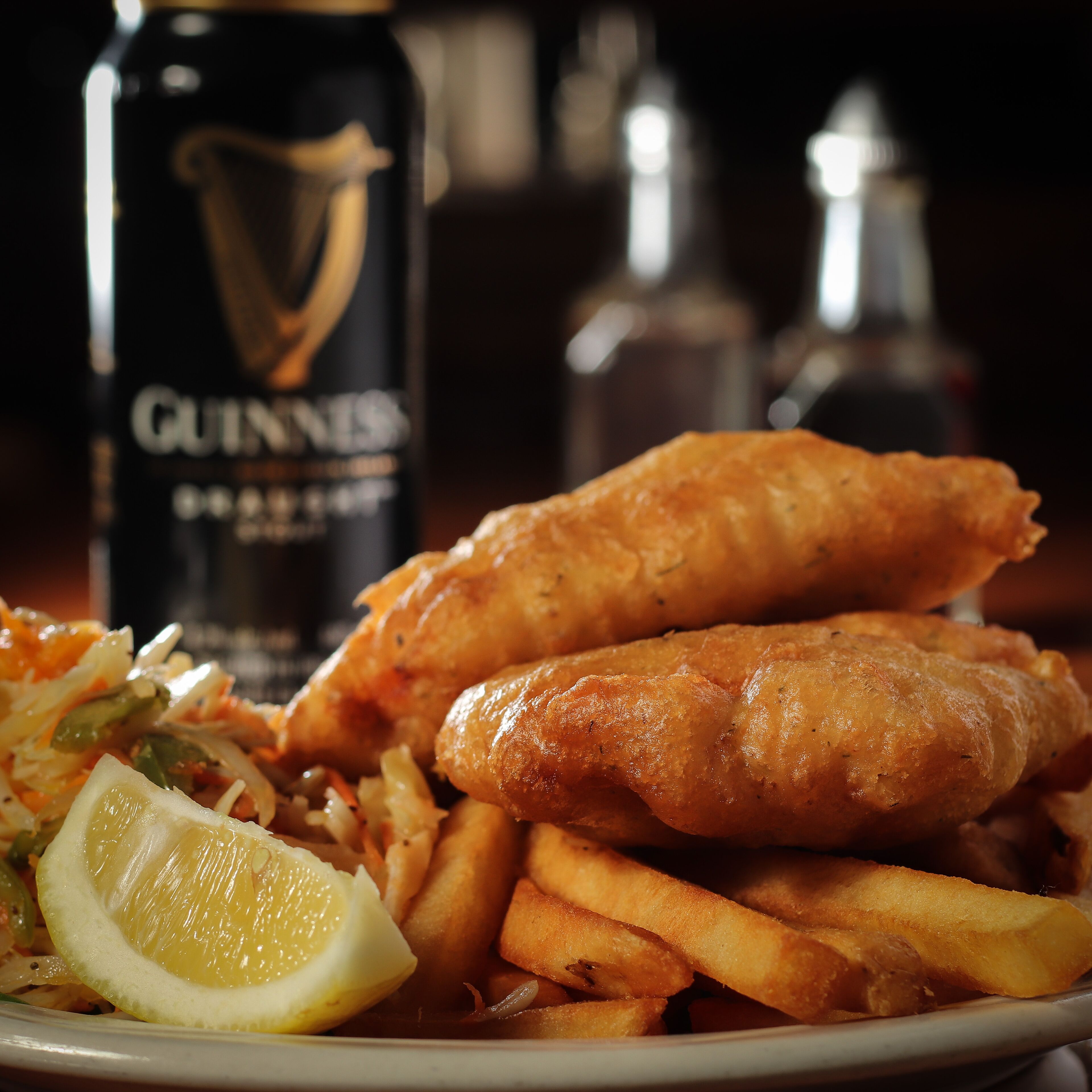 Un plato de pescado con patatas fritas, una rodaja de limón, papas fritas y una botella de cerveza Guinness.