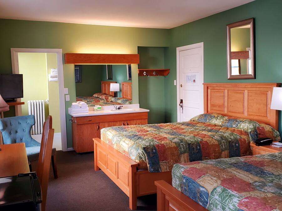 A hotel room with two beds, a wooden dresser, a chair, a desk with a lamp, and a television.