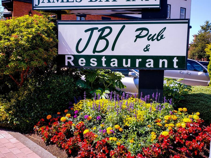 A sign for James Bay Inn, JBI Pub & Restaurant with a flower garden in front.