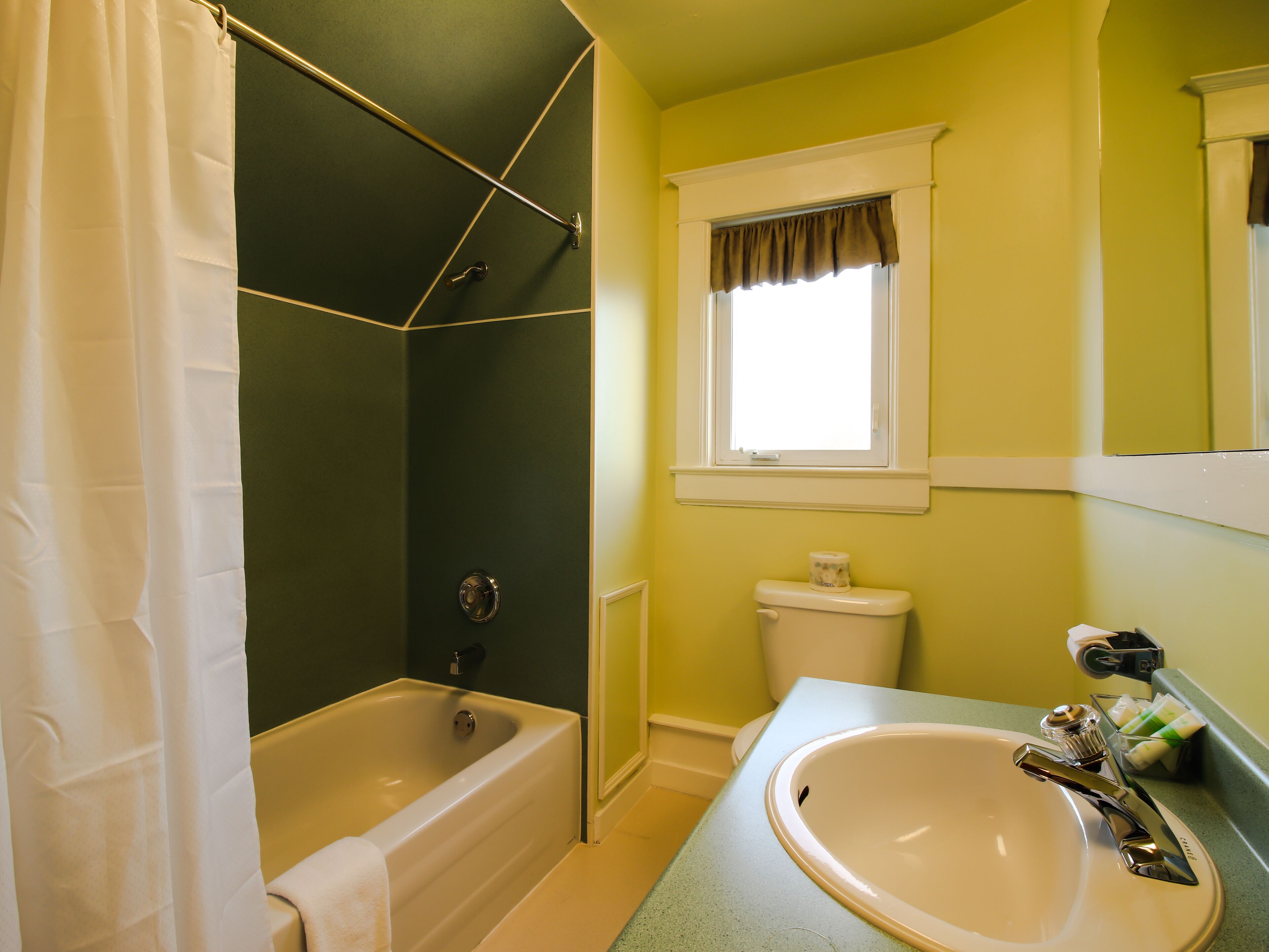 A bathroom with a bathtub, toilet, sink, and a window with a curtain.