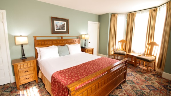 A neatly arranged hotel room with a large bed, two bedside tables with lamps, a chair, and a window with curtains.