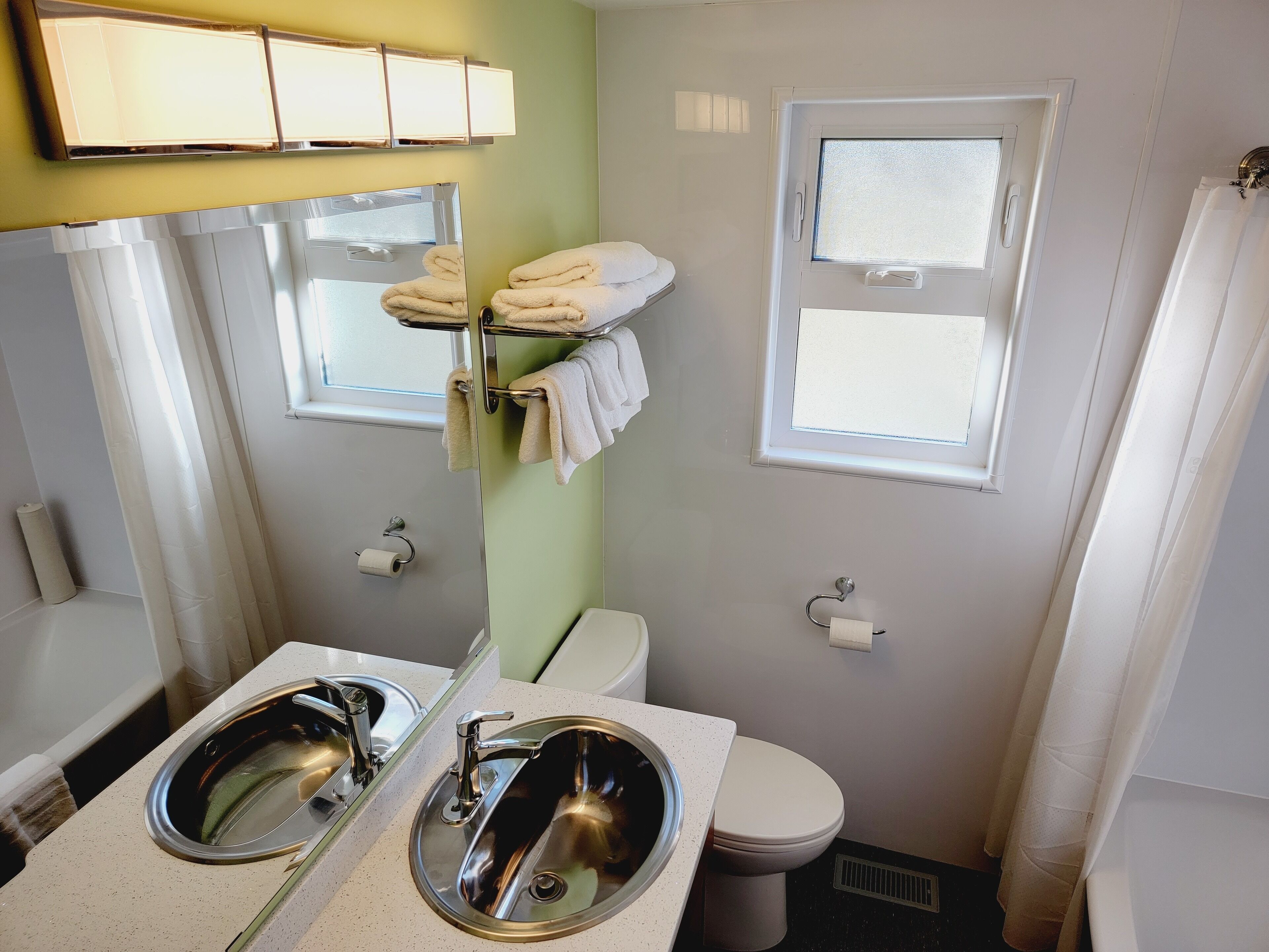 A bathroom with two sinks, a toilet, a towel rack, and a window.