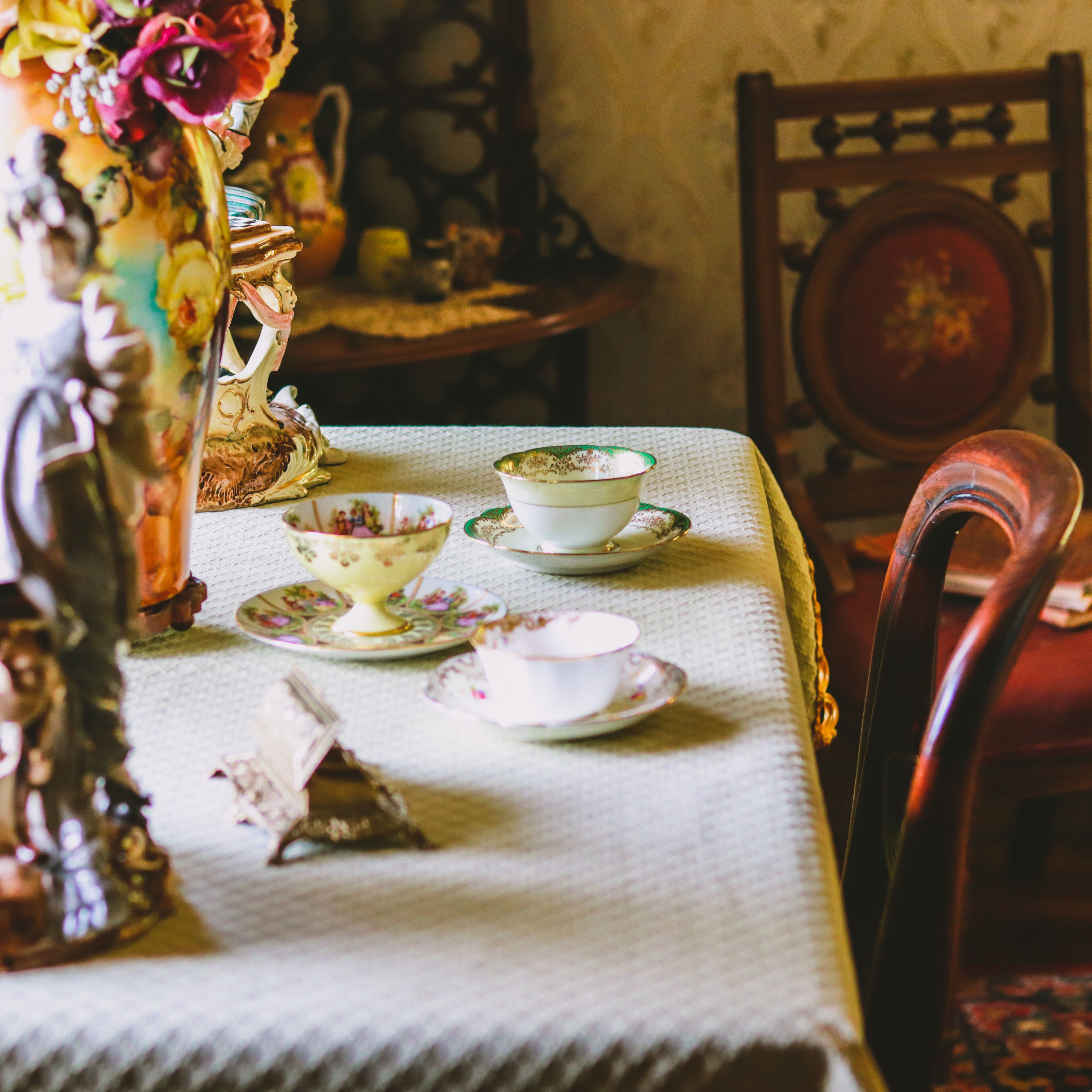 Una mesa de comedor con mantel, un florero con flores, y varios platos y tazas.