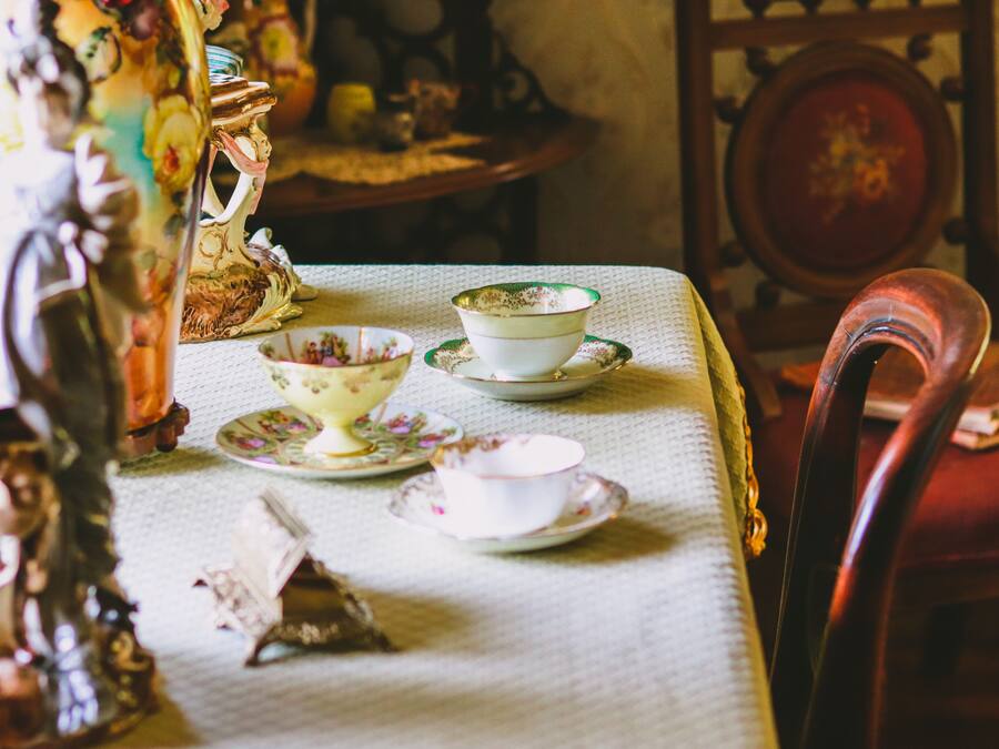 Una mesa de comedor con mantel, un florero con flores, y varios platos y tazas.