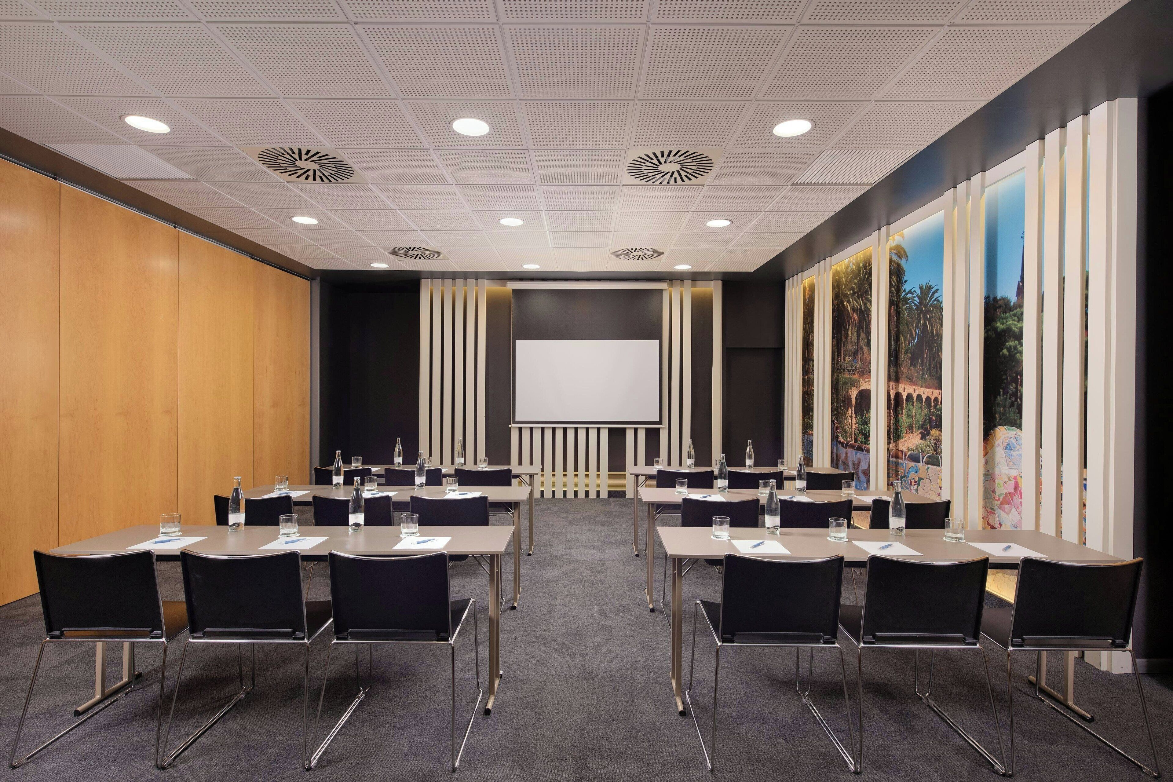A conference room with a large screen, multiple tables, and chairs.