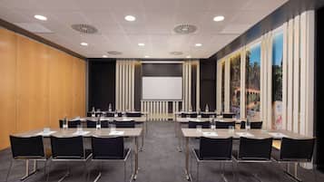 A conference room with a large screen, multiple tables, and chairs.