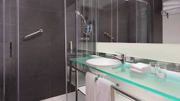 Une salle de bain moderne avec un lavabo en verre, des murs recouverts de carreaux foncés, une cabine de douche en verre et un porte-serviettes.