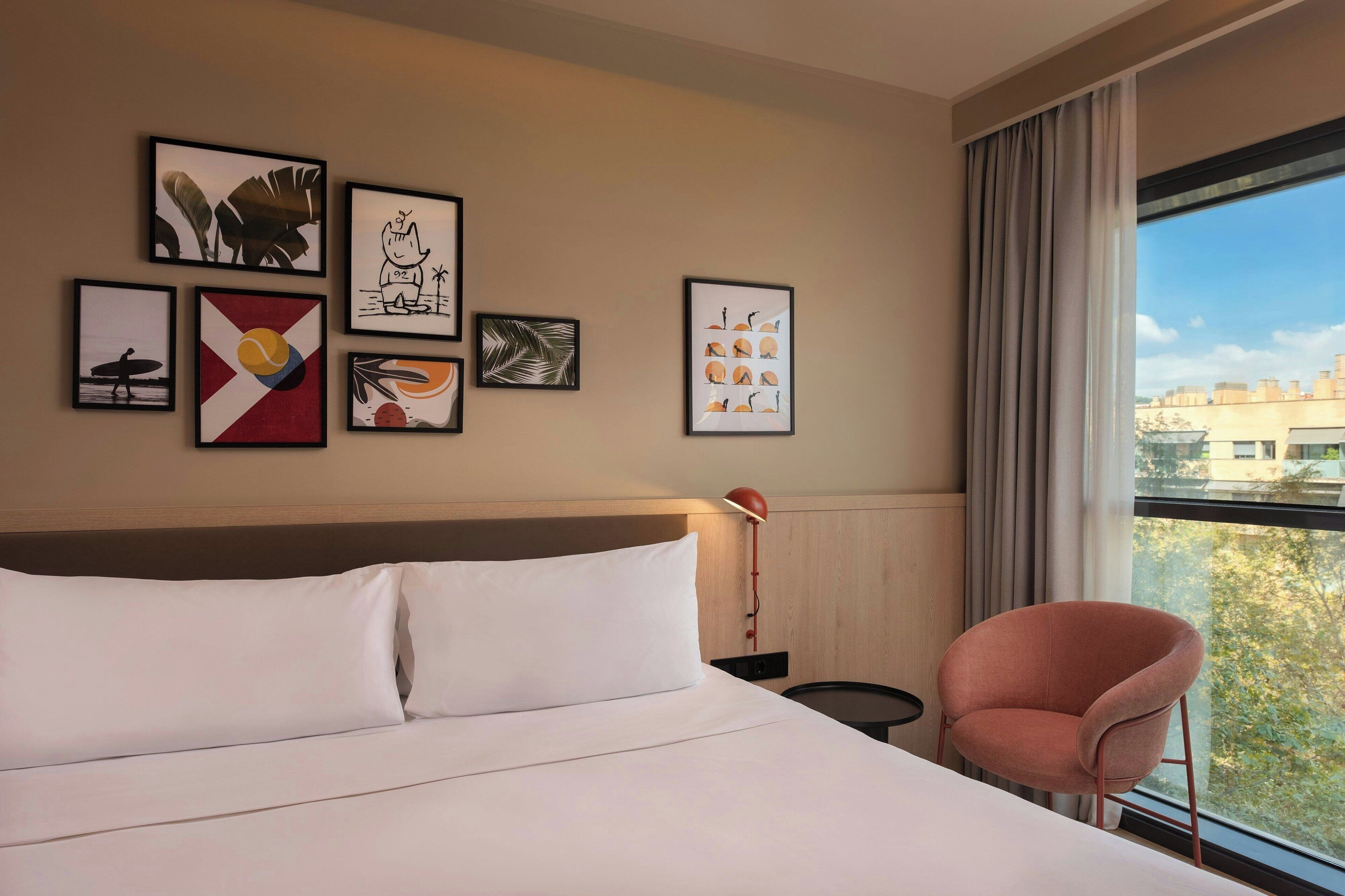 Una habitación de hotel con cama, una silla y obras de arte en la pared.