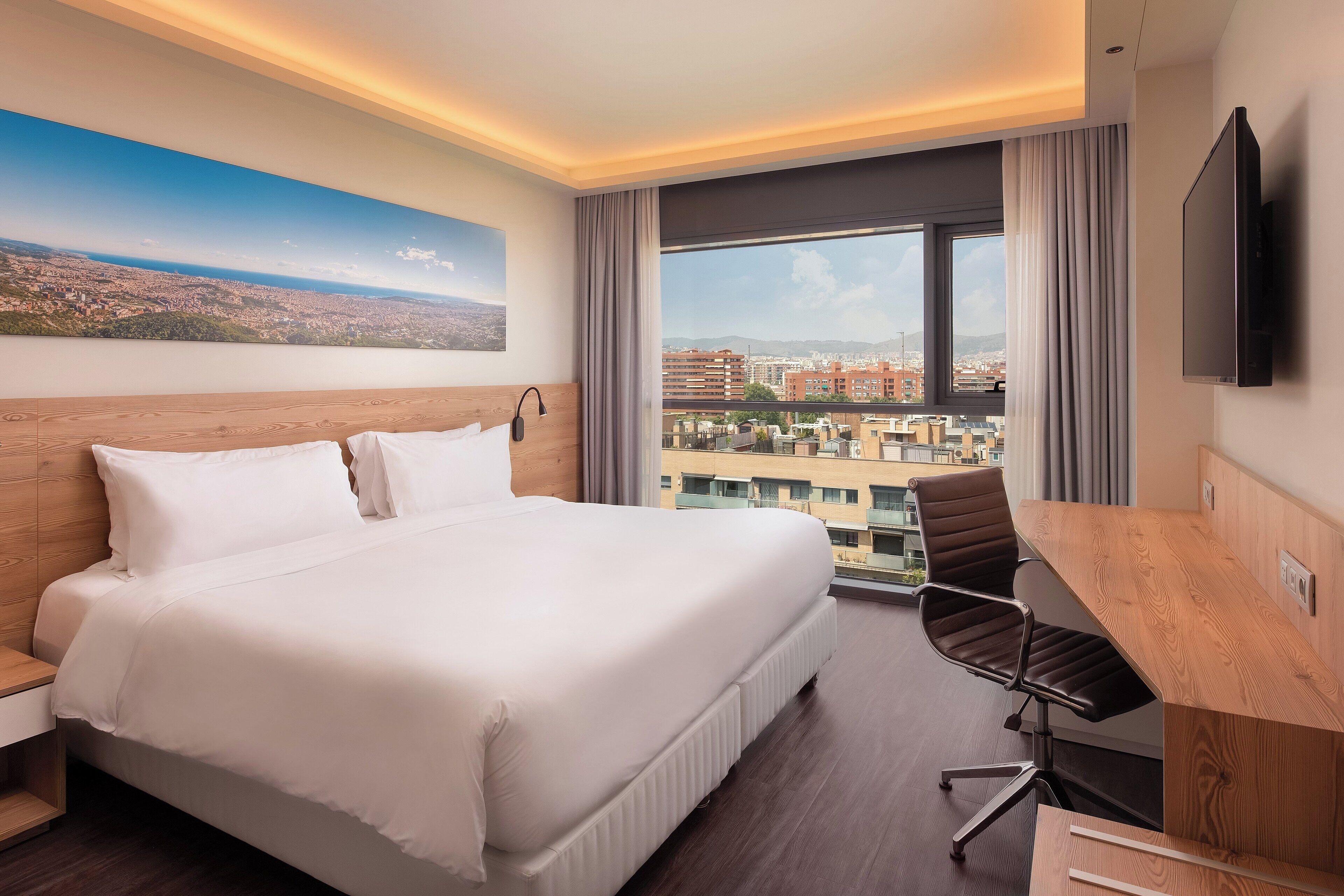 Habitación de hotel con una cama grande, un escritorio y vistas a la ciudad.