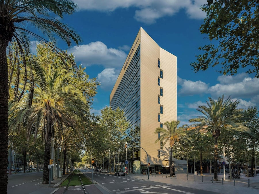 A modern building with a glass facade, surrounded by palm trees and a clear sky.