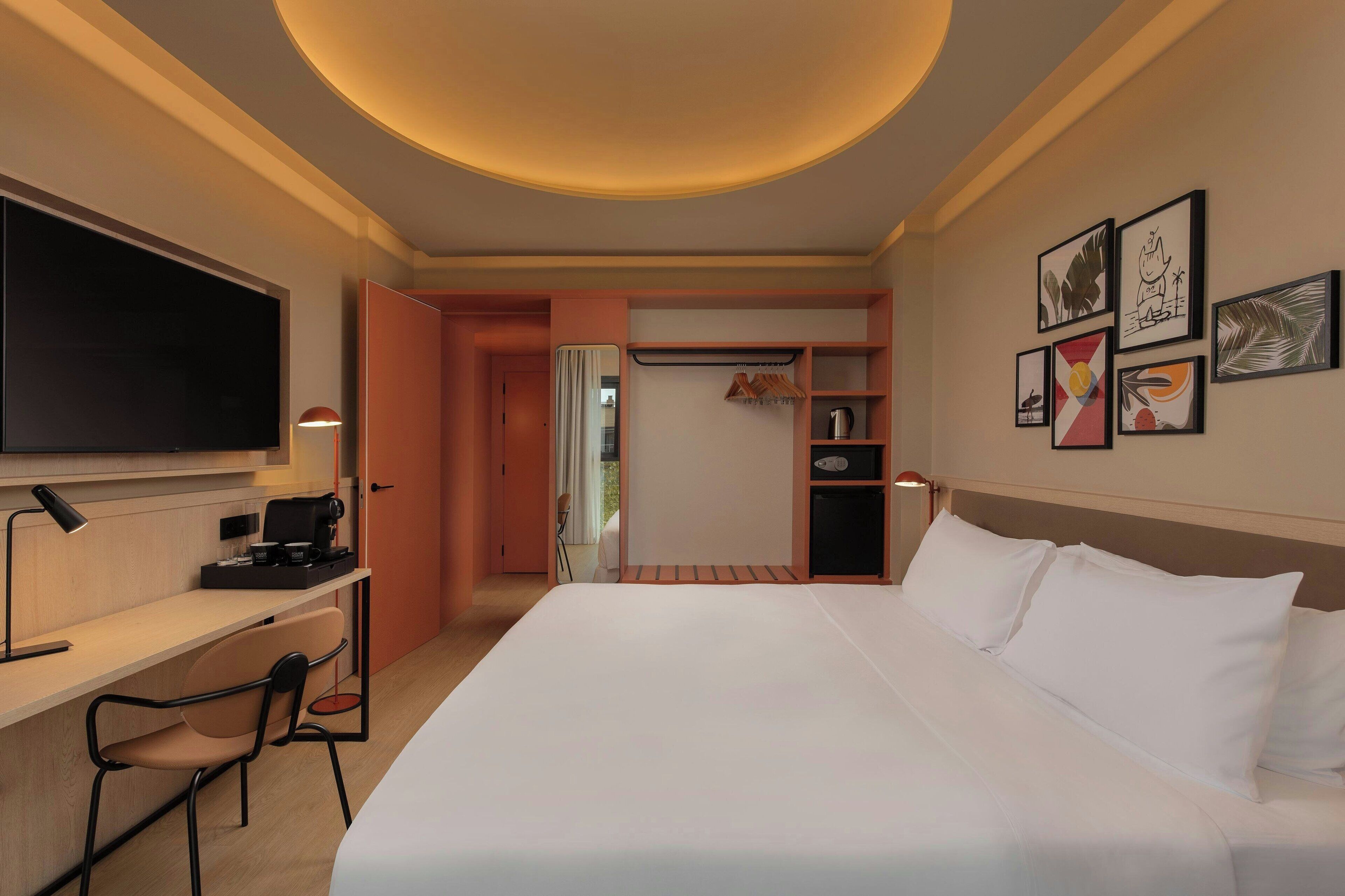Habitación de hotel con una cama grande, un escritorio con silla, un televisor de pantalla plana y un armario con estantes.