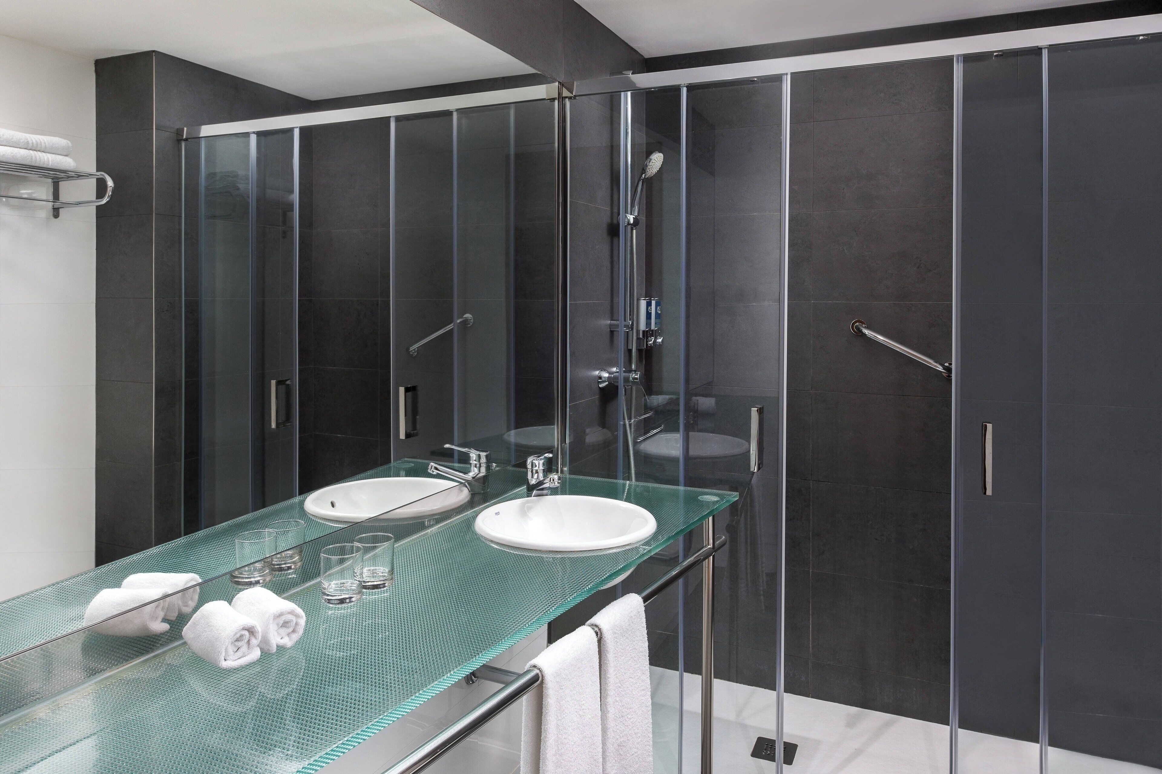 A modern bathroom with two sinks, a glass shower enclosure, and a glass vanity.