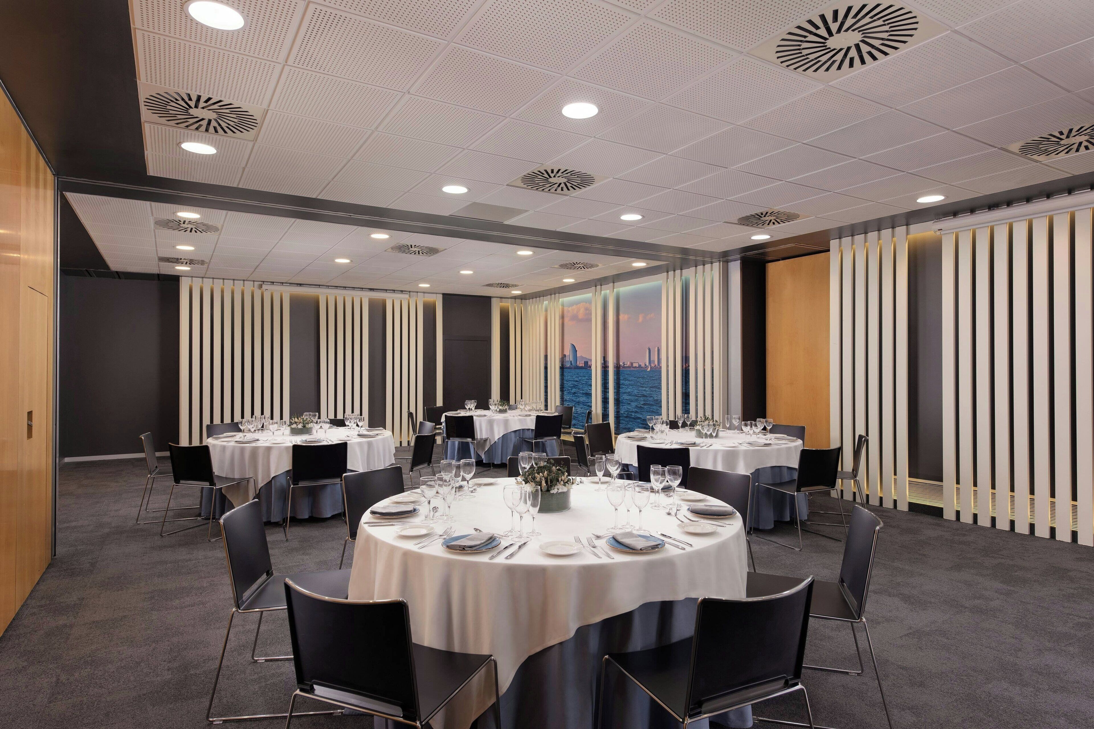 A conference room with round tables, chairs, and a cityscape view through the windows.