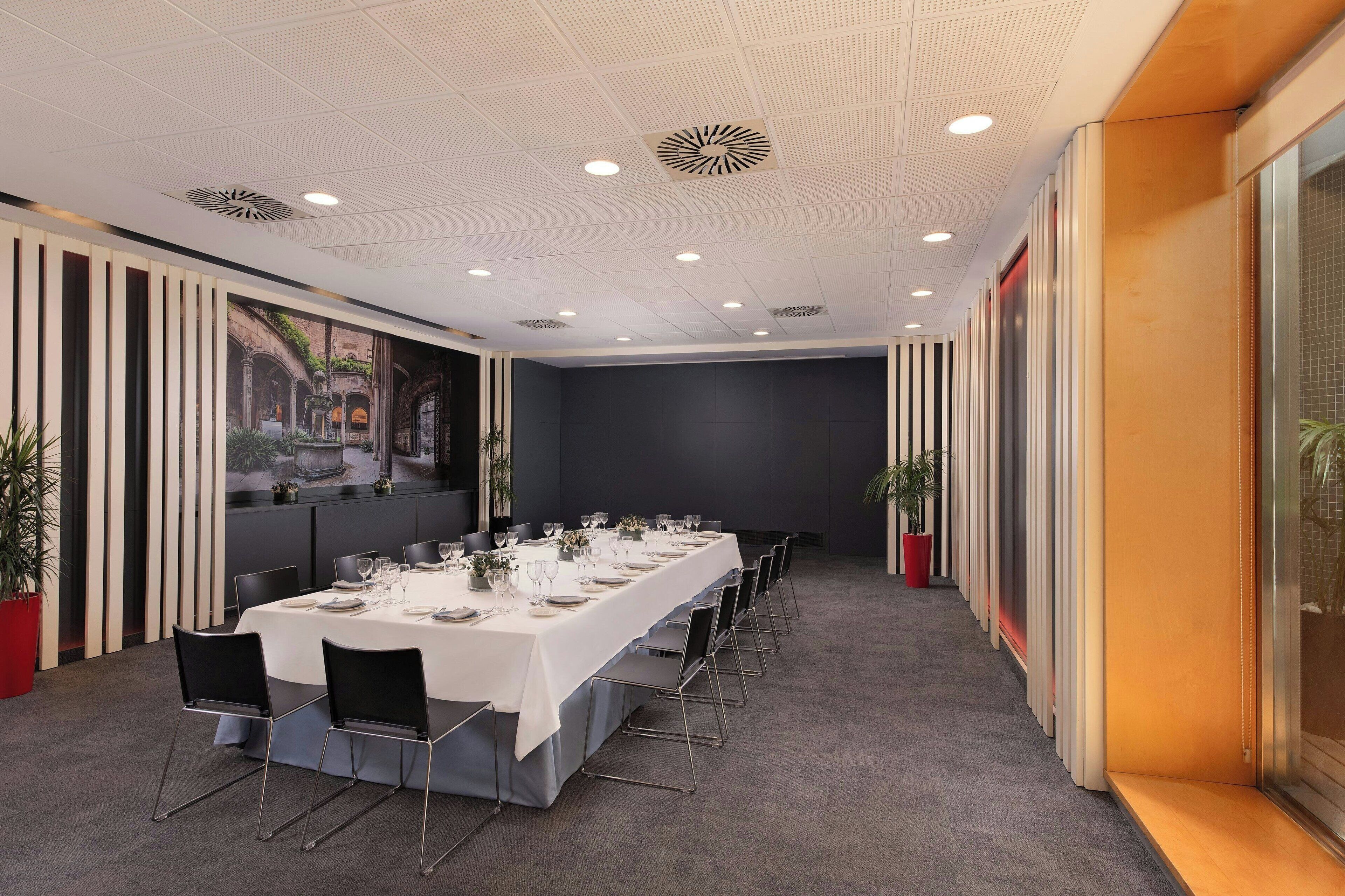 Un salón de conferencias con una larga mesa dispuesta para una reunión, equipado con sillas y una pantalla de proyector.