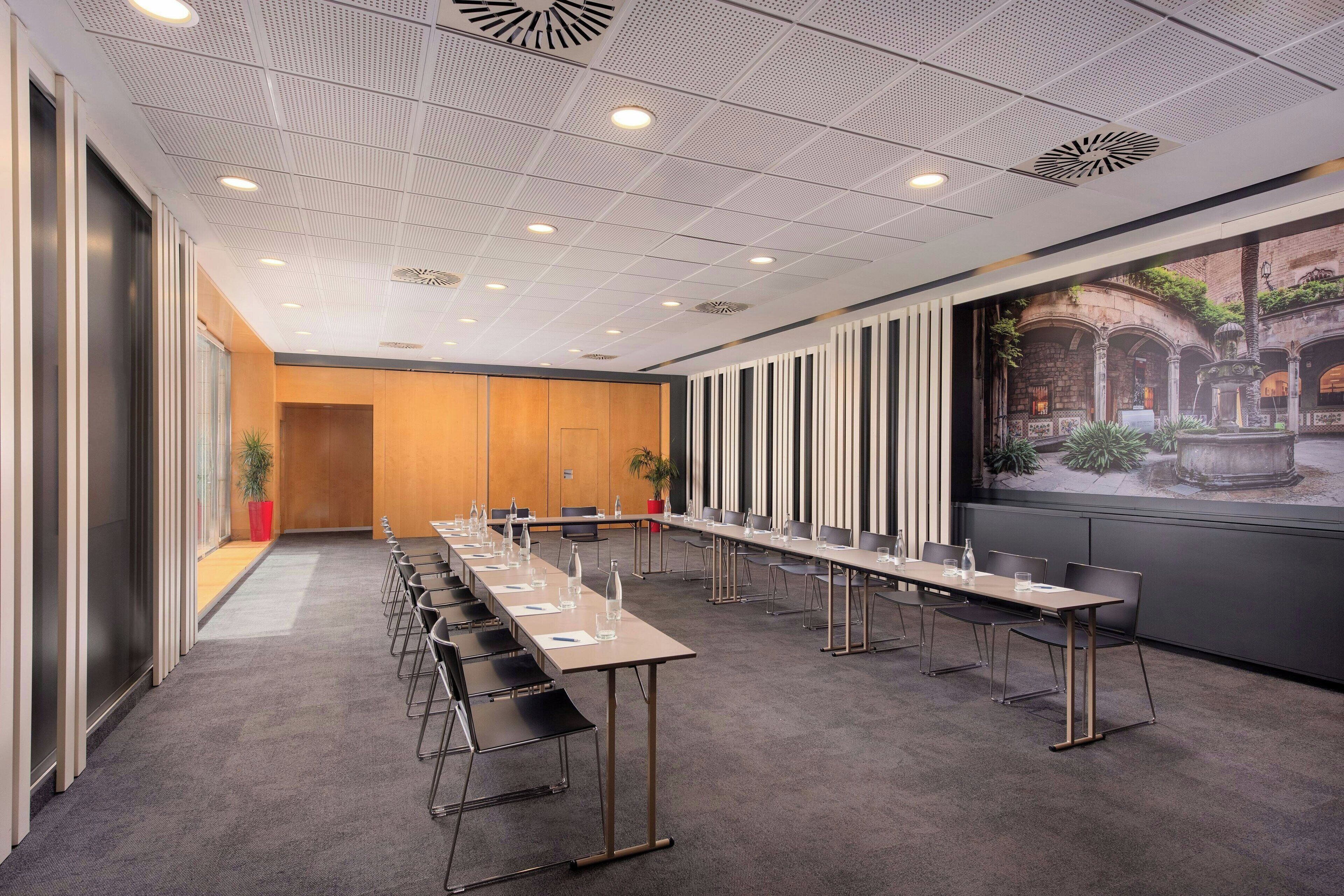 Una sala de conferències amb una taula llarga, cadires i un mural gran a la paret.