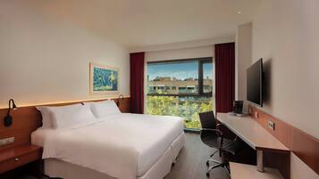 Una habitación de hotel con cama, escritorio, silla, televisión y ventana con vista a la ciudad.