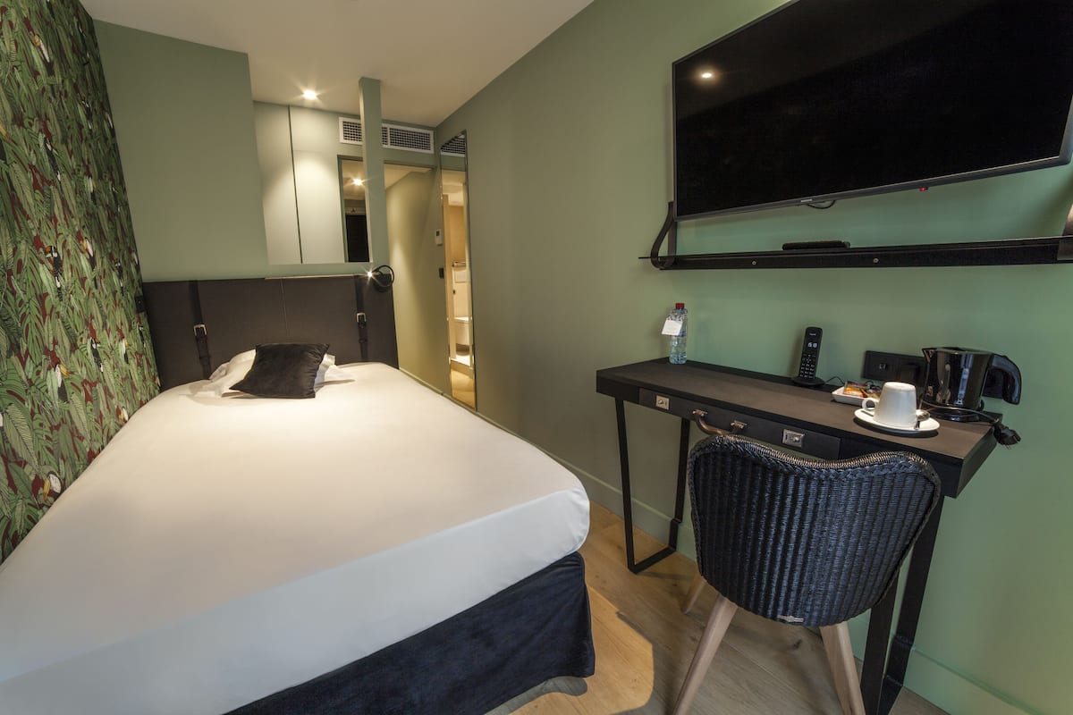 Una habitación de hotel con cama, escritorio, silla, televisor y espejo.
