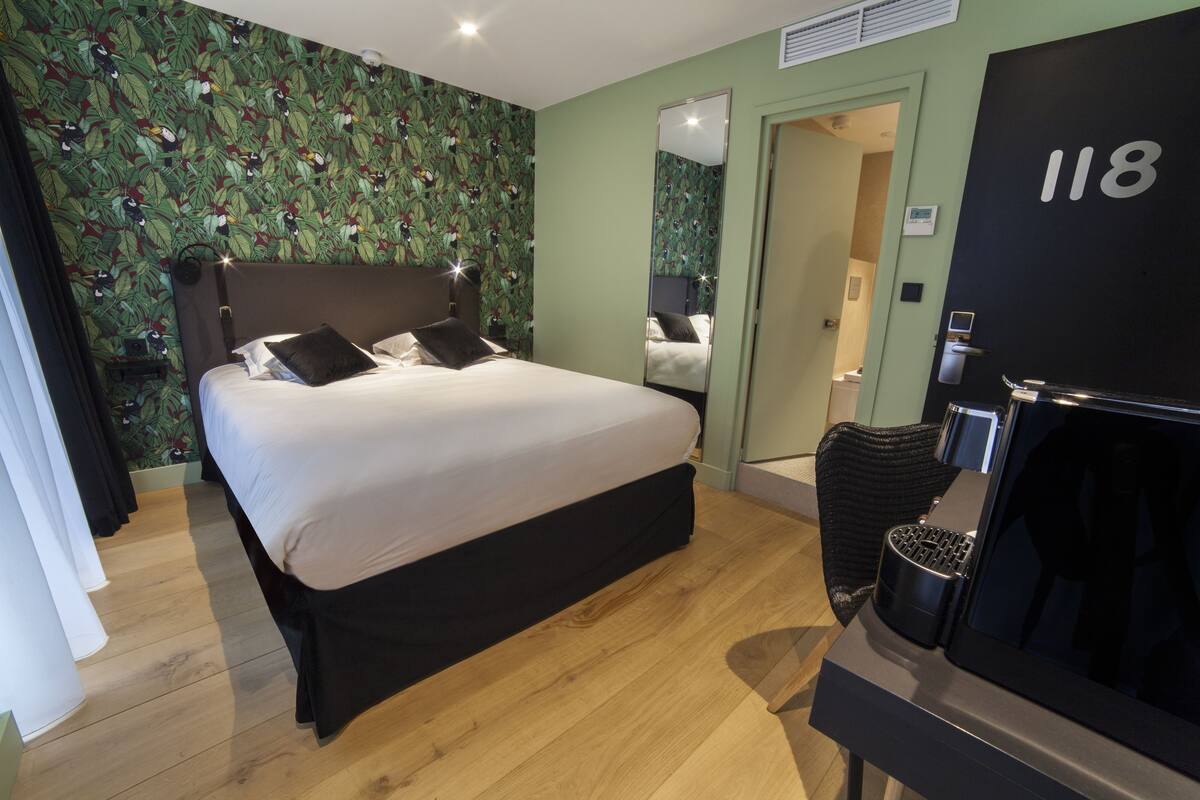 Habitación de hotel con una cama grande, un espejo, una puerta con el número 118 y una silla negra.