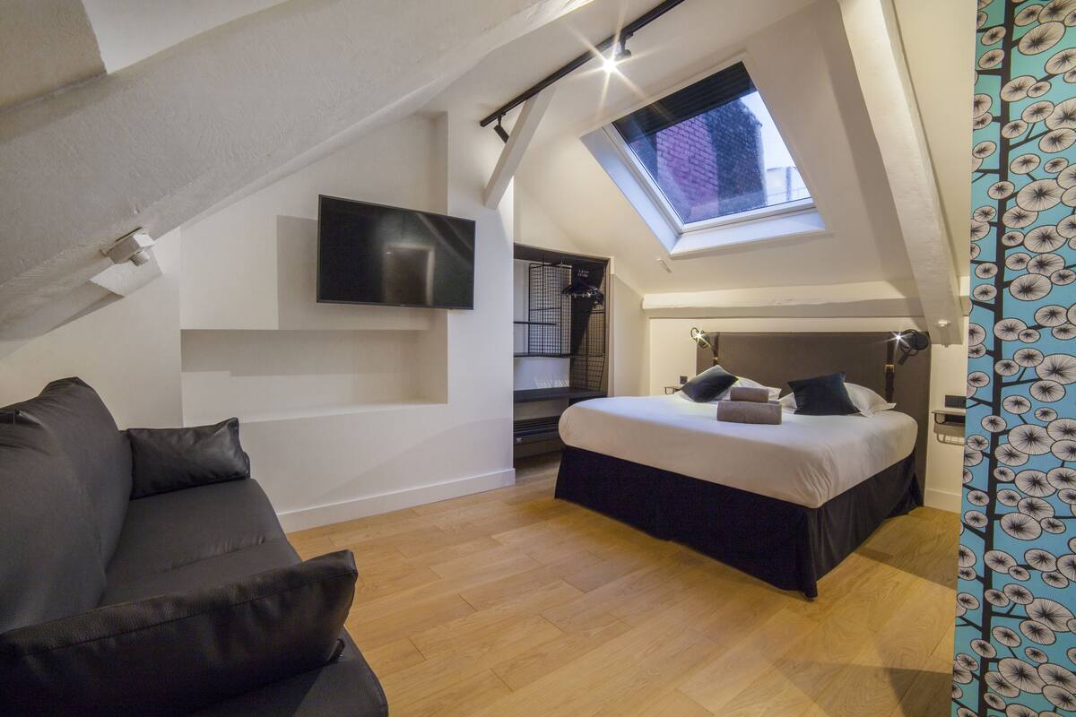 Un dormitorio tipo loft moderno con tragaluces, una cama grande, un televisor de pantalla plana y un sofá.