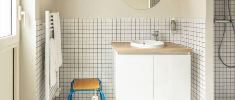 Un baño con un lavamanos blanco, una encimera de madera, un taburete azul y una pared con azulejos.