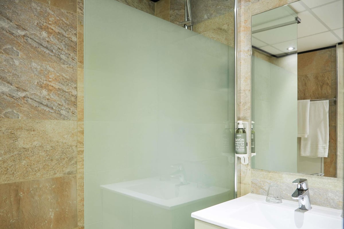 Ein Badezimmer mit Marmorwand, einem weißen Waschbecken, einem Spiegel und einer Duschkabine aus Glas.