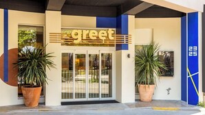 Ingresso di un hotel con un cartello che dice 'greet', grandi piante in vaso e un design moderno con tocchi di blu e beige.