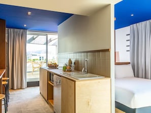 A modern kitchen with a dishwasher, a sink, and a countertop with various items. There is a dining area with chairs and a table, and a bed with a white mattress and pillows. - greet hotel Marseille Parc Chanot Velodrome (Marseille)