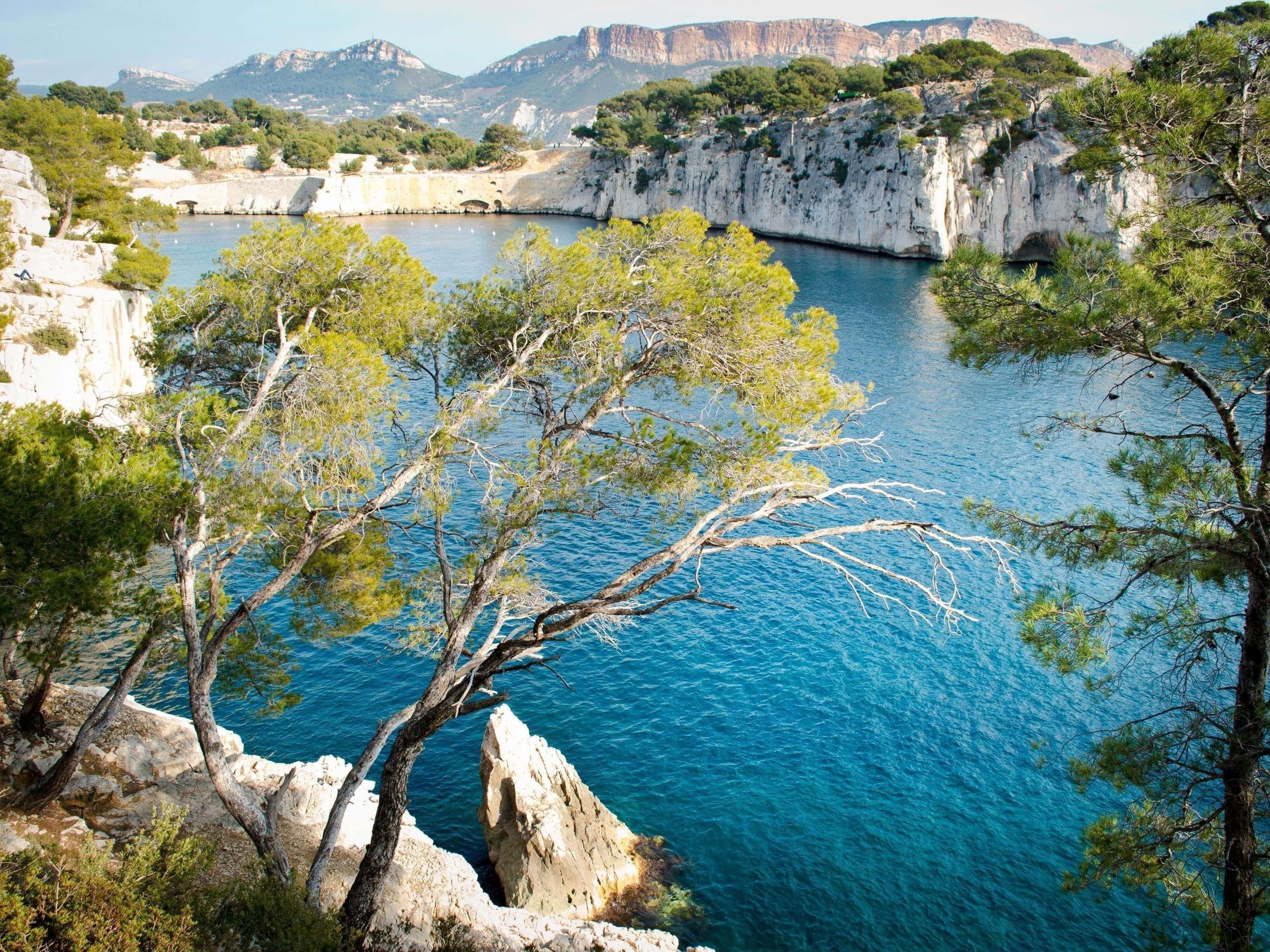A coastal landscape with cliffs, a clear blue sea, and sparse vegetation.
