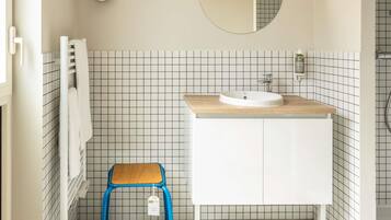 Une salle de bain avec un lavabo blanc, un miroir et un tabouret bleu.