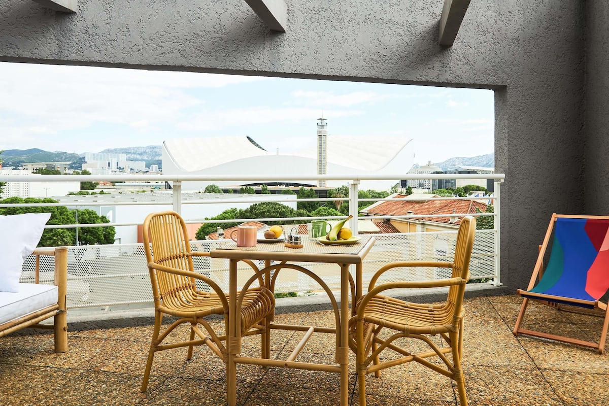 Un balcon avec des fauteuils en osier, une table garnie de nourriture et un tableau.