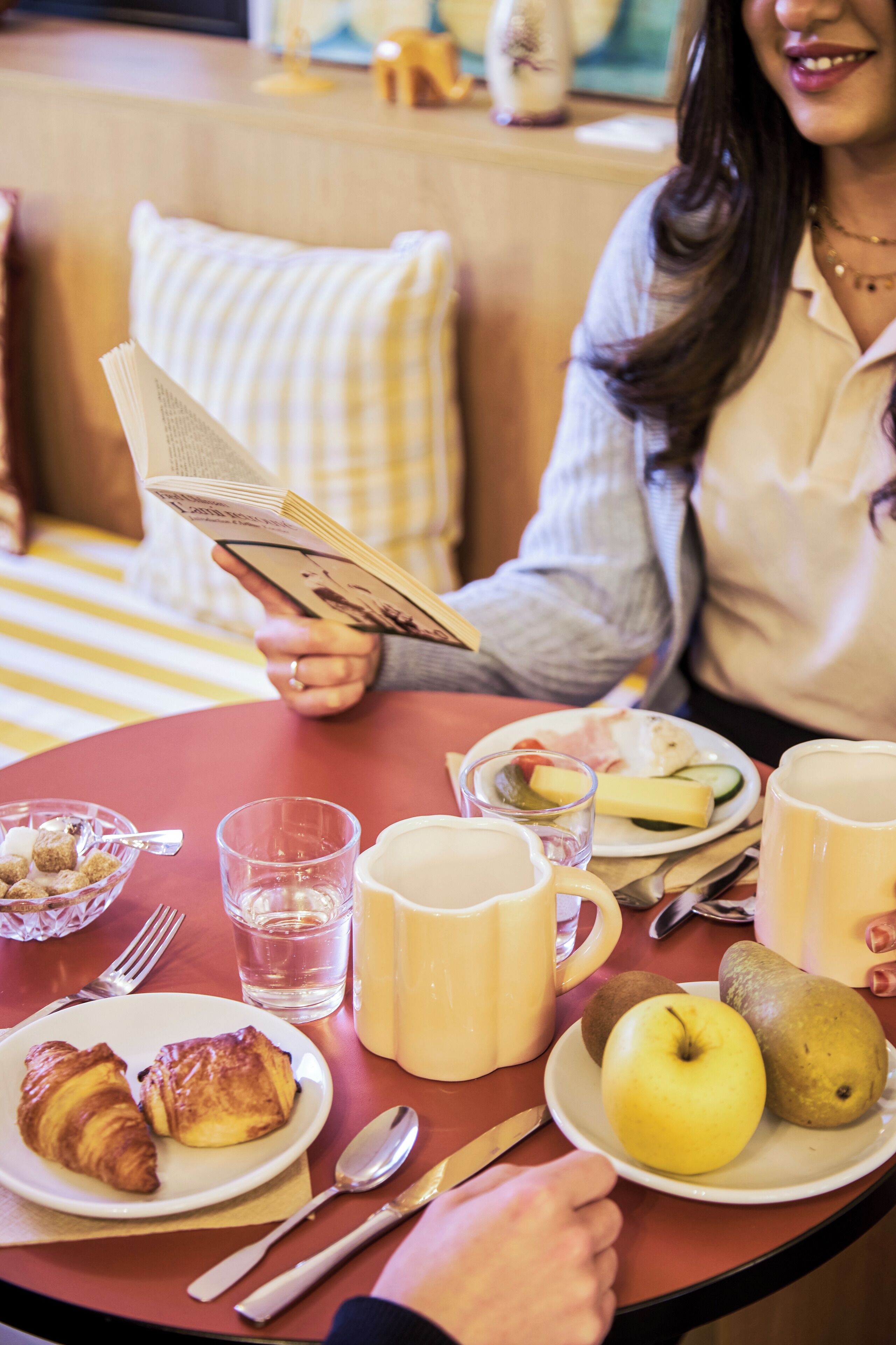 Une table à manger avec une assiette de croissants, un verre d’eau, une tasse et une assiette contenant une pomme et une poire.