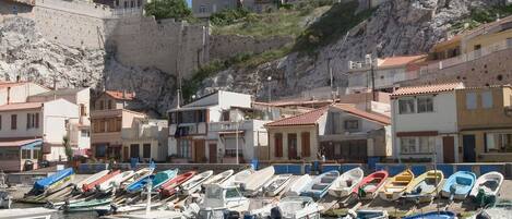 Un puerto deportivo con barcos amarrados, edificios con tejados de tejas rojas y una ladera rocosa al fondo.