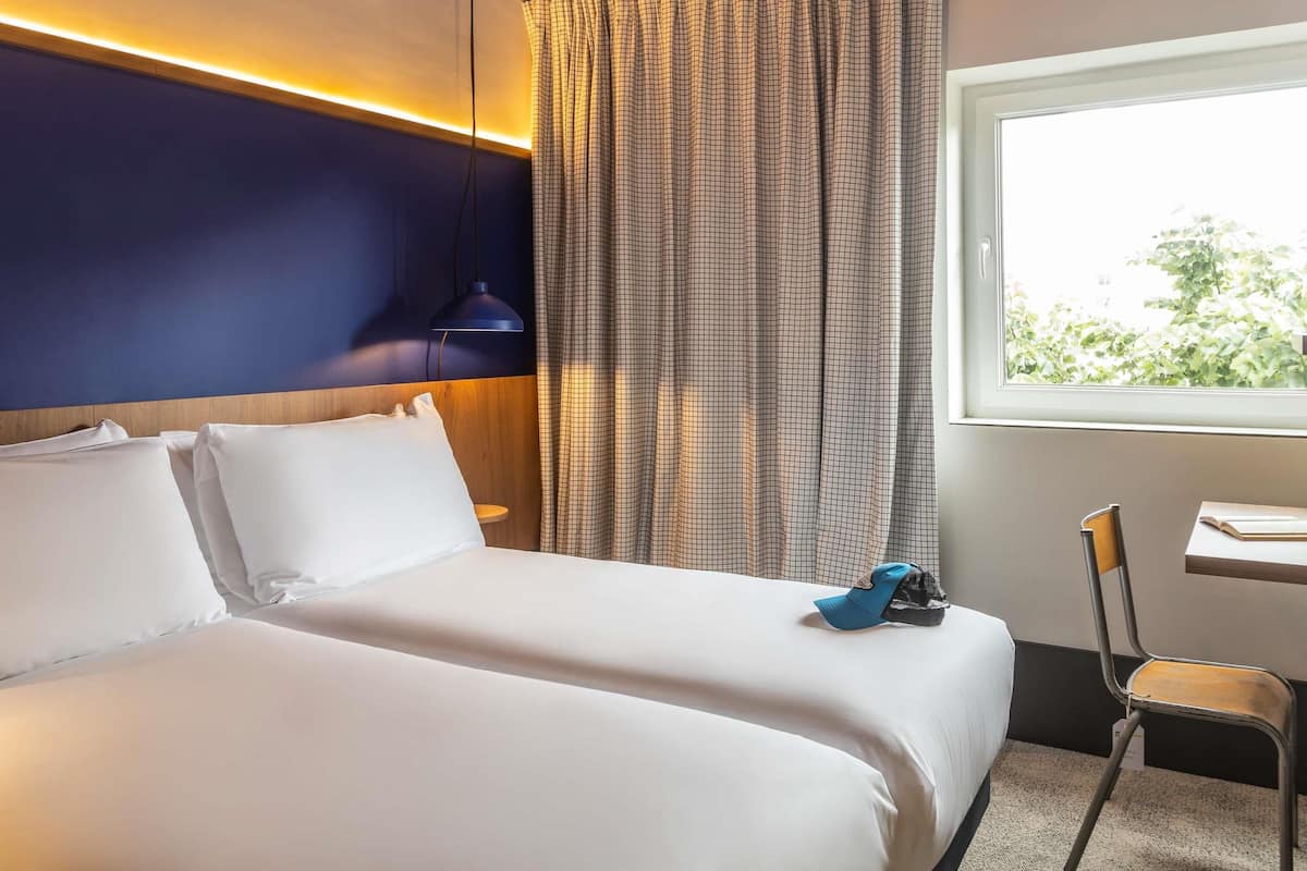 Une chambre d’hôtel équipée d’un lit, d’un bureau, d’une chaise et d’une fenêtre donnant sur un paysage verdoyant.