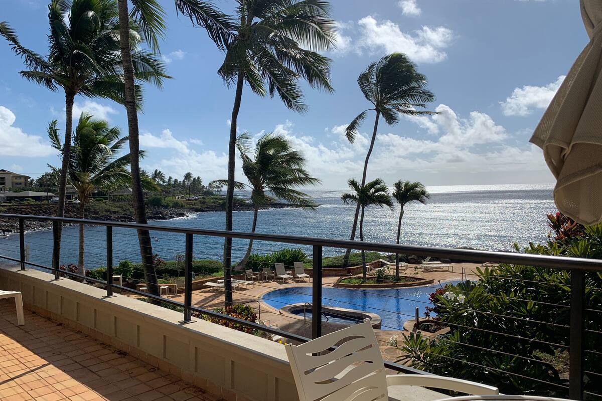 A balcony with a view of a swimming pool, palm trees, and the ocean.