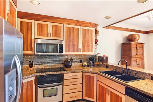 A kitchen with wooden cabinets, a stainless steel refrigerator, a microwave, an oven, a dishwasher, and a granite countertop.