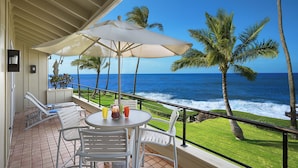A balcony with a table, chairs, and an umbrella overlooking the ocean.