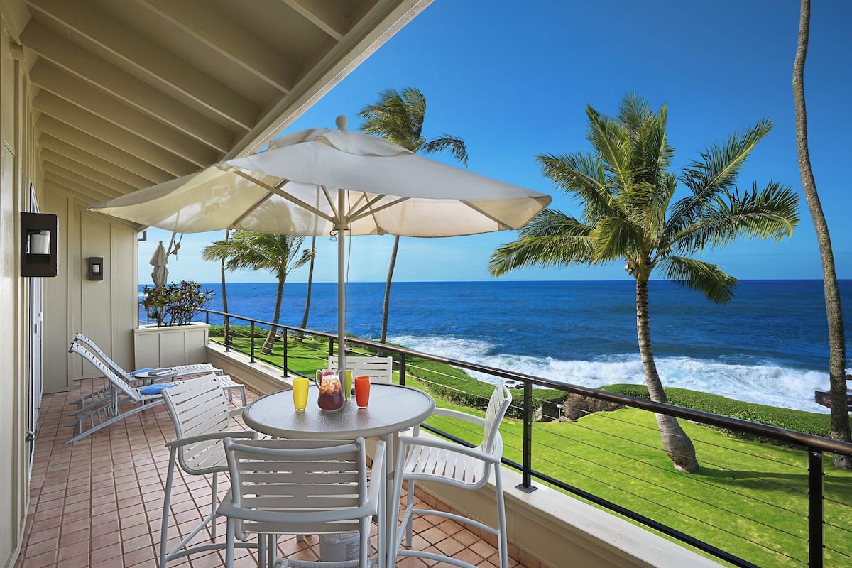 A balcony with a table, chairs, and an umbrella overlooking the ocean.
