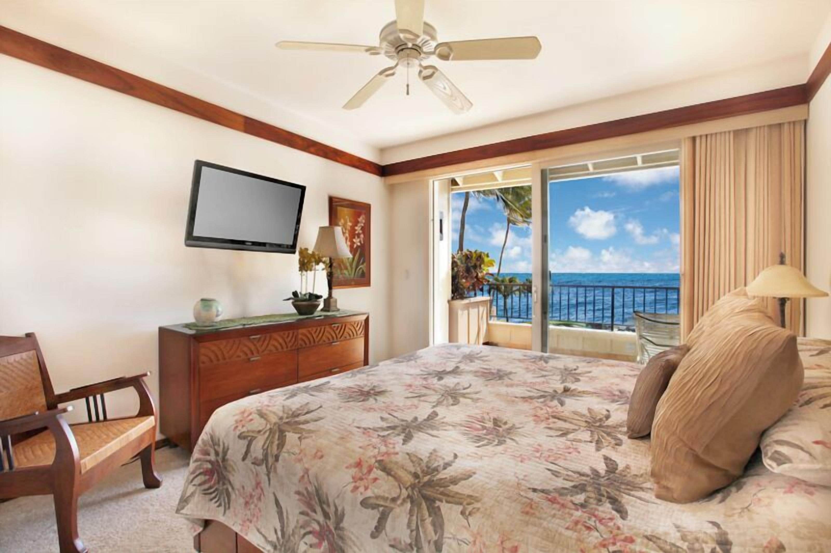 A hotel room with a bed, a television, a desk, and a view of the ocean.