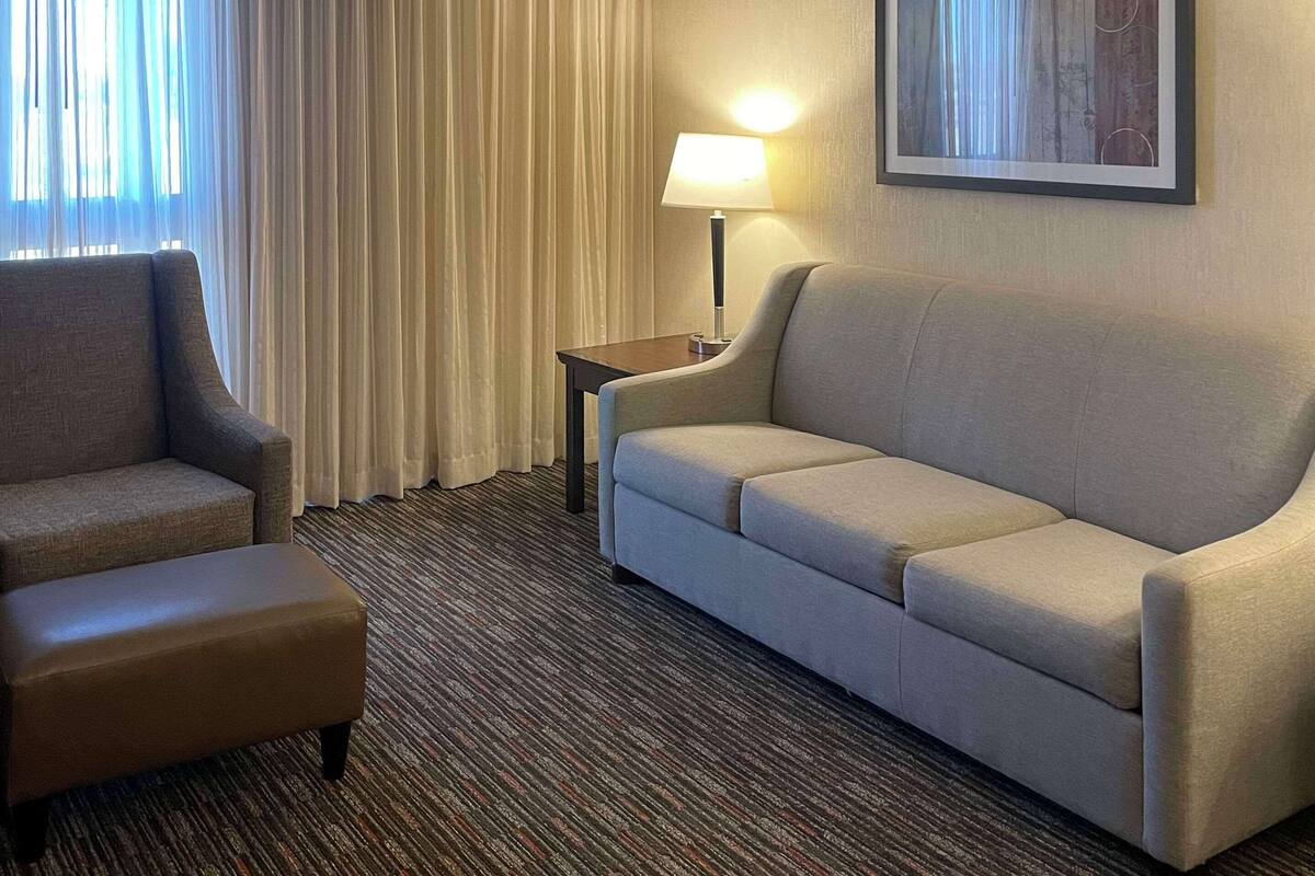 A hotel room with a sofa, armchair, and a lamp on a side table.