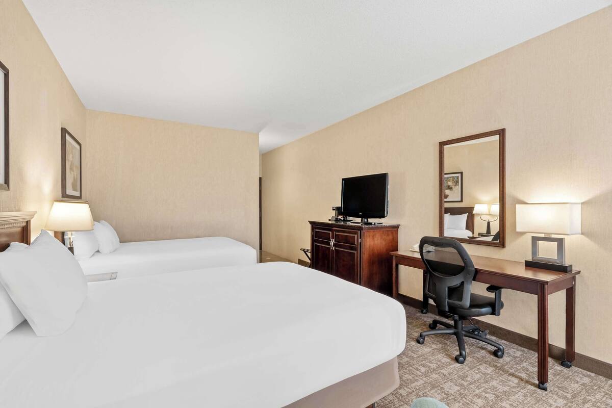 A hotel room with two single beds, a desk with a chair, a television, and a mirror.