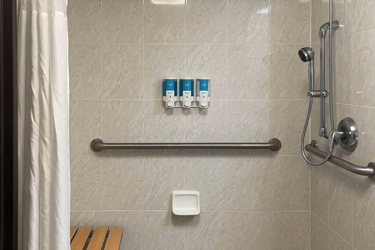 A shower area with a grab bar, a handheld showerhead, and three blue soap dispensers on the wall.